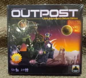 The image shows the box cover of the "OUTPOST 20th Anniversary Deluxe Edition" board game by James Hlavaty, featuring sci-fi artwork with alien figures and a space landscape, with a sun and planet in the background. The box also indicates the game includes "Tom Lehmann's Kicker Expansion," is for players aged 12 and up, and accommodates 2-9 players. The Stronghold Games logo is visible in the bottom right corner.