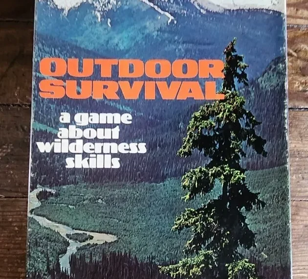 A board game titled "OUTDOOR SURVIVAL - a game about wilderness skills" with an image of a forested landscape and snow-capped mountains in the background.