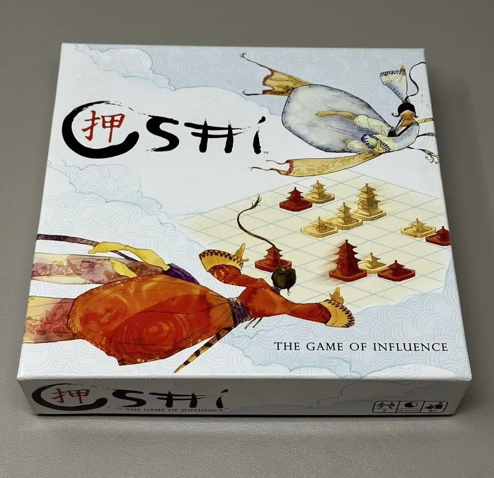 Image of a board game titled "SHŌBU" with the subtitle "THE GAME OF INFLUENCE" on the box cover, which features artistic depictions of a flying egret carrying a stone while a crawfish with a human-like posture observes a chessboard pattern with game pieces, set against a background with wave patterns.