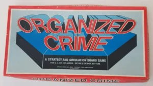 The image shows the cover of a board game titled "ORGANIZED CRIME," described as a strategy and simulation game for four, three, or two players, with further details on the box bottom, and it is by KOPLOW GAMES, Billerica, Mass. The copyright date is 1973 James Koplow. The background is red with a blue 3D box graphic design.