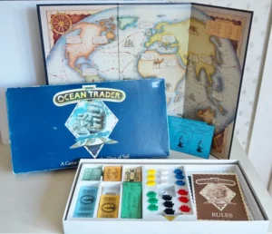 A "Ocean Trader" board game with its box lid, game board, colorful money bills, ship pieces, cards, and rule book displayed on a table.
