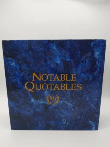 A book with a deep blue marbled cover titled "Notable Quotables" with a golden emblem below the text.