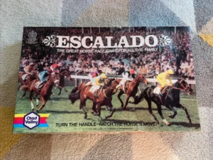 Box cover of "Escalado - The Great Horse Race Game for All the Family" by Chad Valley, depicting a close-up scene of horse racing with jockeys, placed on a patterned fabric surface.