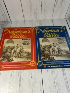 Two boxed board game expansions titled "Napoleon's Battles", Module One (red box) and Module Two (blue box), by The Avalon Hill Game Company, placed side by side on a white wooden surface. Both covers feature illustrations of Napoleonic era soldiers and riders on horseback.