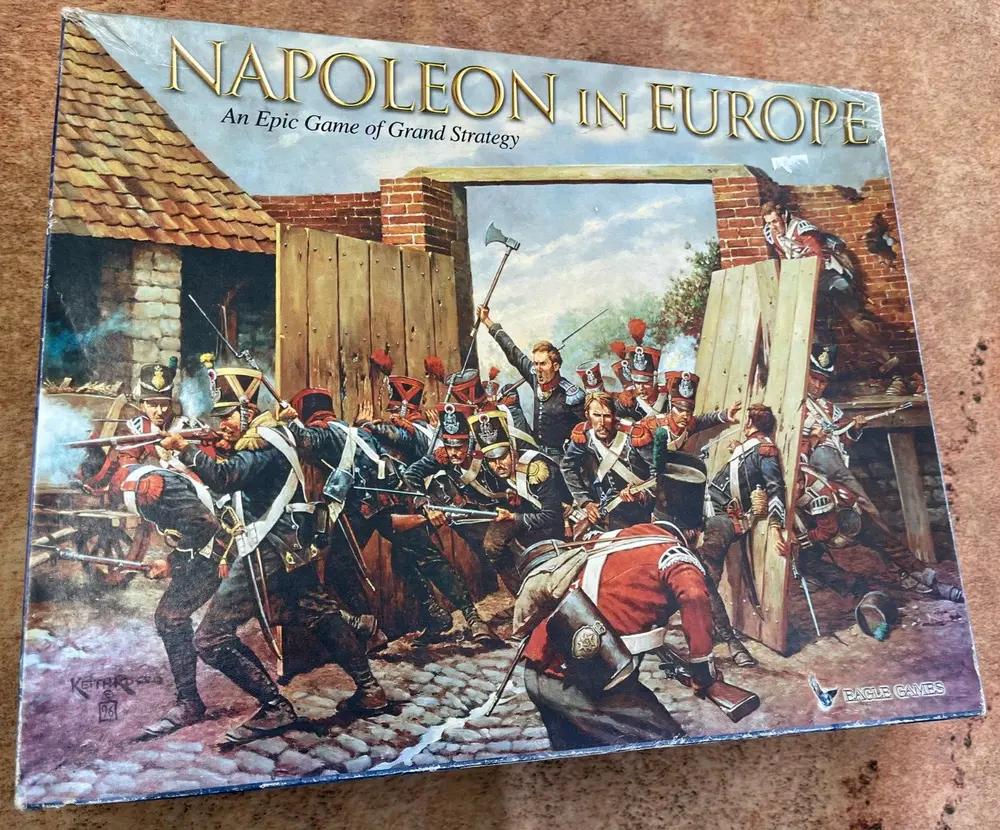 A board game box cover for "NAPOLEON IN EUROPE: An Epic Game of Grand Strategy" featuring a dynamic illustration of Napoleonic-era soldiers in combat by a damaged building, with one soldier prominently leading a charge. The corner of the image shows the logo of Eagle Games and the signature of the artist, "Keith Rocco '96."
