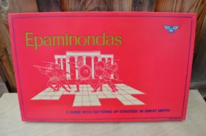 A board game box titled "Epaminondas" with a graphic of ancient warriors and a chessboard pattern, the tagline reads "A GAME WITH PATTERNS OF STRATEGY IN GREAT DEPTH". A small blue winged logo appears in the top right corner.