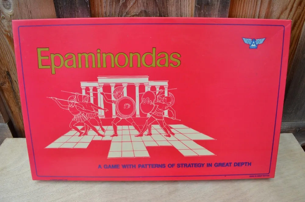 A board game box titled "Epaminondas" with a graphic of ancient warriors and a chessboard pattern, the tagline reads "A GAME WITH PATTERNS OF STRATEGY IN GREAT DEPTH". A small blue winged logo appears in the top right corner.