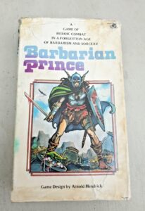 A worn tabletop game book titled "Barbarian Prince," with artwork of a helmeted warrior holding a sword and shield on the cover. The subtitle reads "A GAME OF HEROIC COMBAT IN A FORGOTTEN AGE OF BARBARISM AND SORCERY." "Game Design by Arnold Hendrick" is noted at the bottom.