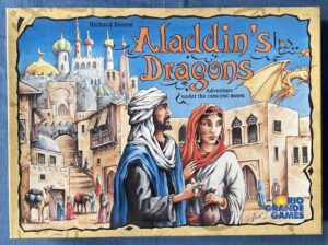 The image shows the cover of a board game titled "Aladdin's Dragons" by Richard Breese, depicting a colorful, illustrated scene with a Middle Eastern cityscape and a man and woman in traditional clothing in the foreground. There is a dragon flying in the sky above the city, and the text mentions an "Adventure under the crescent moon." The Rio Grande Games logo is displayed in the bottom right corner.