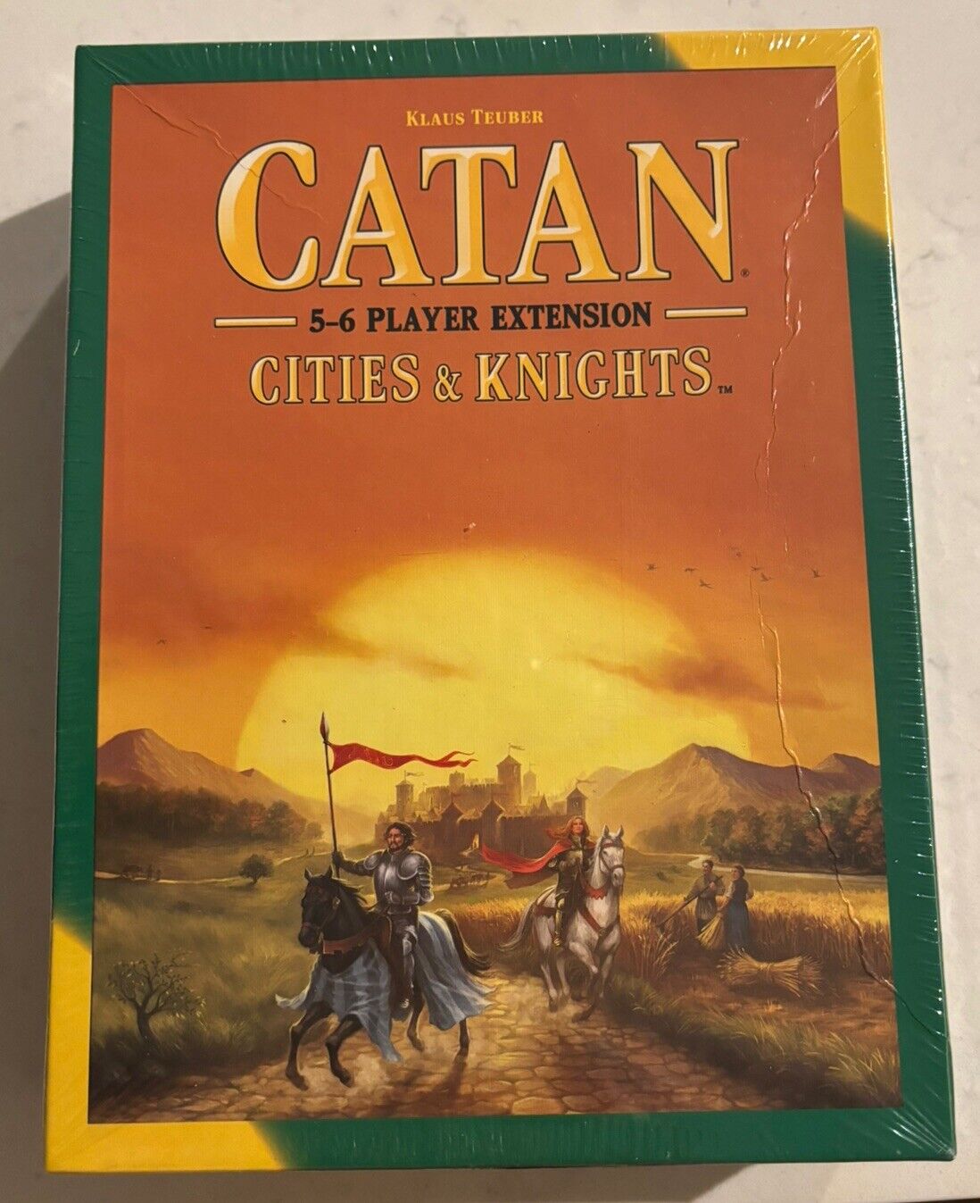 The image displays a sealed box of "CATAN 5-6 Player Extension Cities & Knights Board Game" with artwork featuring medieval knights on horses against a backdrop of a countryside at sunset.
