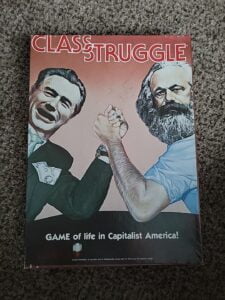 "Board game cover titled 'CLASS STRUGGLE' featuring caricature illustrations of two men arm wrestling, with one man representing capitalists and the other representing workers, and the subtitle 'GAME of life in Capitalist America!'"
