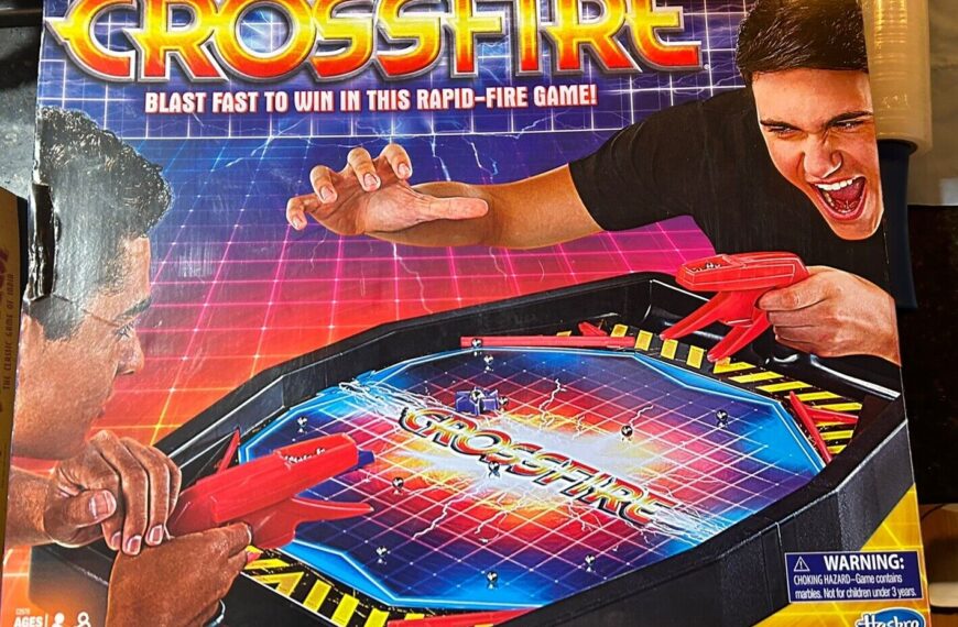 Box cover of the Crossfire board game, featuring intense graphics with two players holding red plastic guns aiming at game pieces on the board, with the slogan "Blast fast to win in this rapid-fire game!" Visible age recommendation is 7+ and a warning label for choking hazard. The Hasbro Gaming logo is in the bottom right corner.