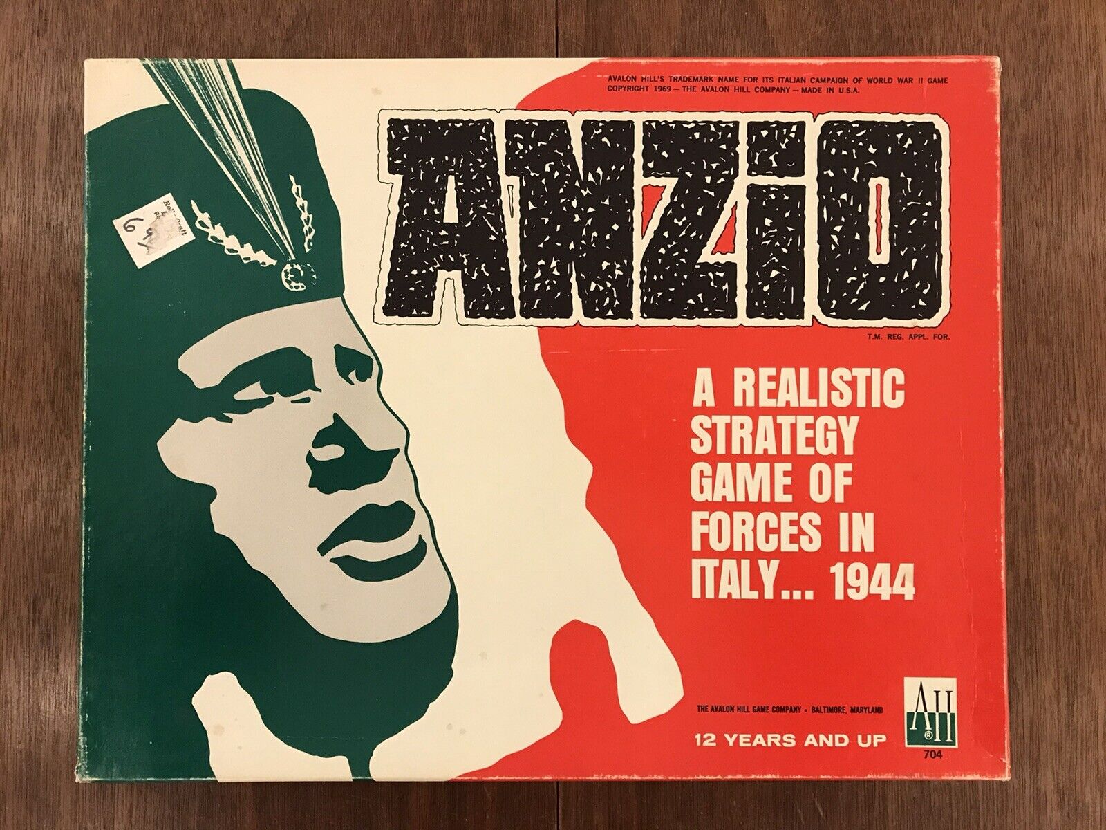 Vintage "ANZIO" board game cover featuring a stylized green and white soldier profile with the title text in large distressed black letters on a red background, subtitled "A Realistic Strategy Game of Forces in Italy... 1944," and additional information including the age suitability "12 years and up," the Avalon Hill Game Company logo, and a product number "704."
