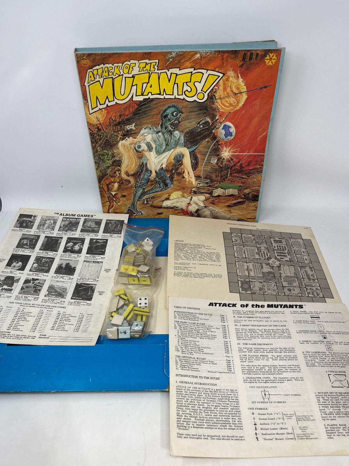 "Attack of the Mutants" board game box with artwork depicting a blue mutant, along with game pieces, dice, and instructional papers spread out on a white surface.