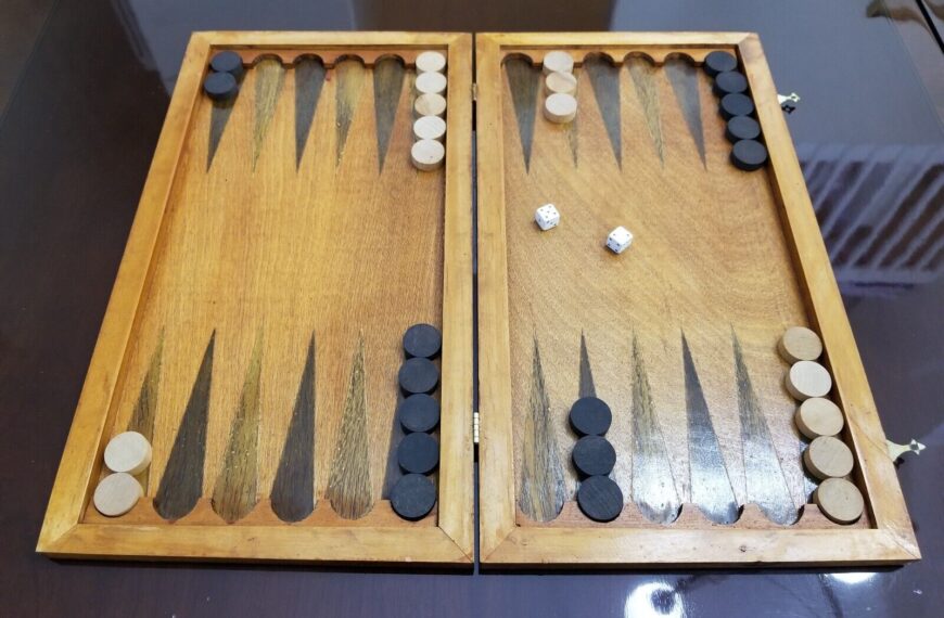 A wooden backgammon board with a game in progress, showing black and white checkers scattered across the board and a pair of dice showing five and one.