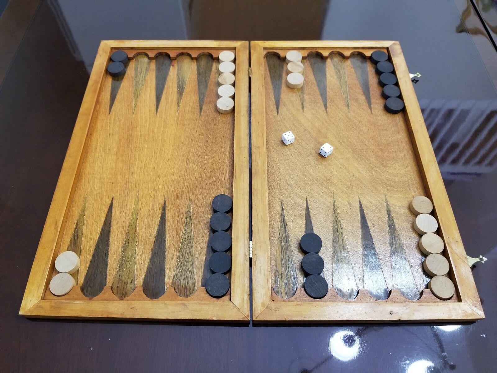 A wooden backgammon board with a game in progress, showing black and white checkers scattered across the board and a pair of dice showing five and one.