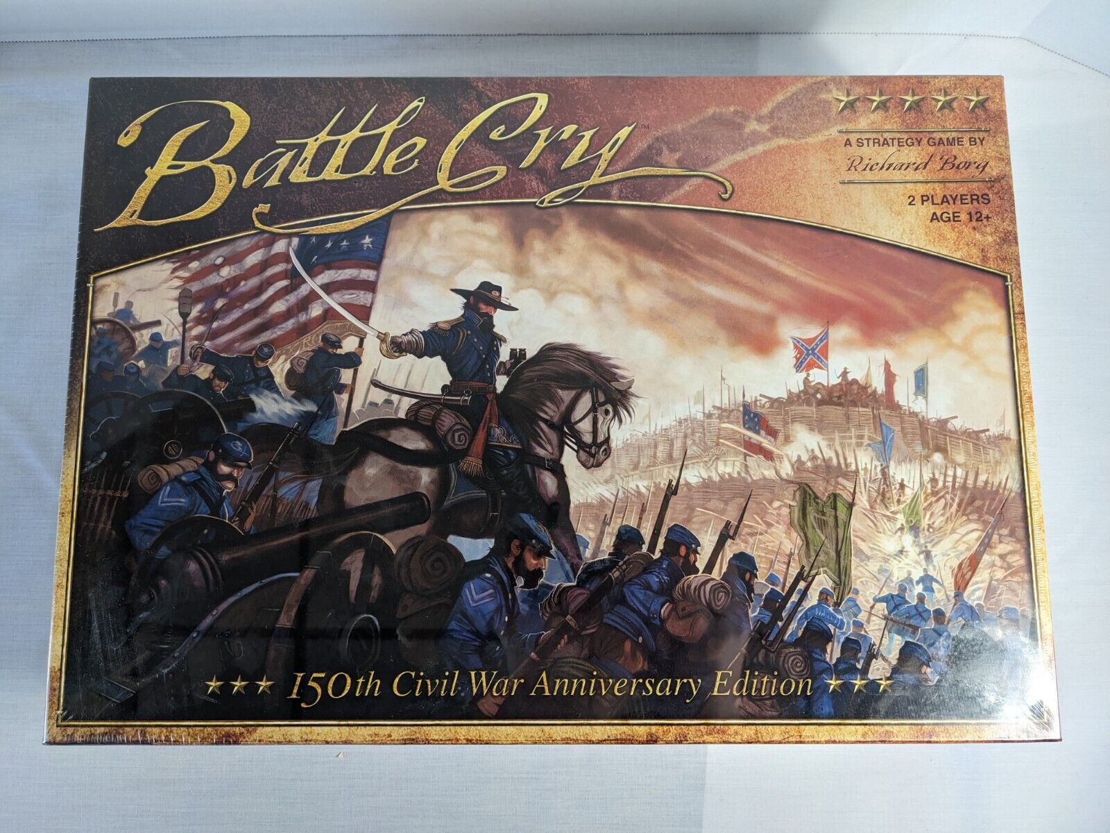 Alt text: The image shows the box cover of "Battle Cry: 150th Civil War Anniversary Edition," a strategy board game by Richard Borg for 2 players aged 12+. The cover art features a dynamic Civil War battle scene with soldiers in blue uniforms, some on horseback, carrying the American flag, and a backdrop of a battlefield with flags and smoke.
