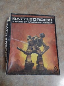 A worn copy of the "BATTLEDROIDS: A GAME OF ARMORED COMBAT" tabletop game box featuring a large robotic mech on a fiery backdrop. The FASA Corporation logo is visible in the bottom right corner.