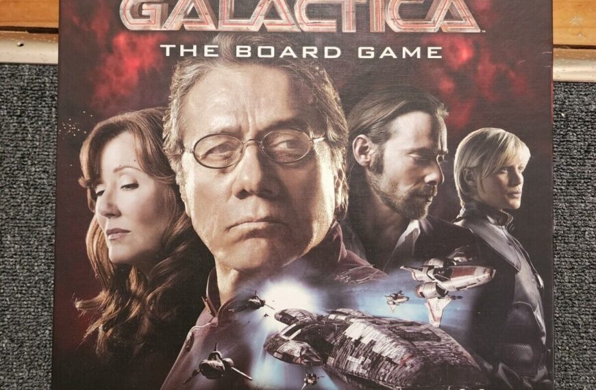 The image shows a "Battlestar Galactica: The Board Game" box lying on a carpeted floor against a wooden threshold. The cover features portraits of characters from the show above a depiction of the Battlestar Galactica spaceship, space fighters, and the tagline "A GAME OF POLITICS, BETRAYAL, AND SURVIVAL." The Syfy channel logo is in the bottom right corner, indicating their affiliation.