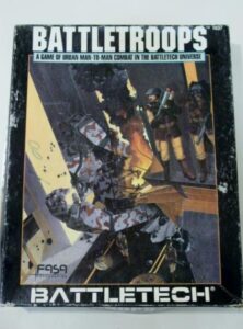 A worn copy of the "BATTLETROOPS" board game box with the subtitle "A GAME OF URBAN MAN-TO-MAN COMBAT IN THE BATTLETECH UNIVERSE," featuring stylized artwork of futuristic soldiers in combat on the cover. The FASA and BATTLETECH logos are visible at the bottom.
