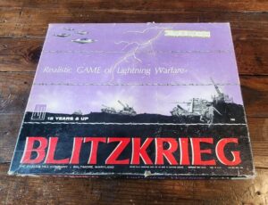 A worn board game box labeled "BLITZKRIEG" with the subtitle "Realistic GAME of Lightning Warfare" for ages "12 YEARS & UP," featuring military imagery, by THE AVALON HILL COMPANY, BALTIMORE, MARYLAND, displayed on a wooden surface.