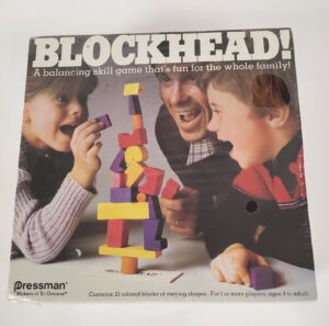 A vintage "BLOCKHEAD!" board game cover featuring two kids and an adult excitedly playing with a stack of colorful wooden blocks, with text indicating it is a balancing skill game for the whole family by Pressman.