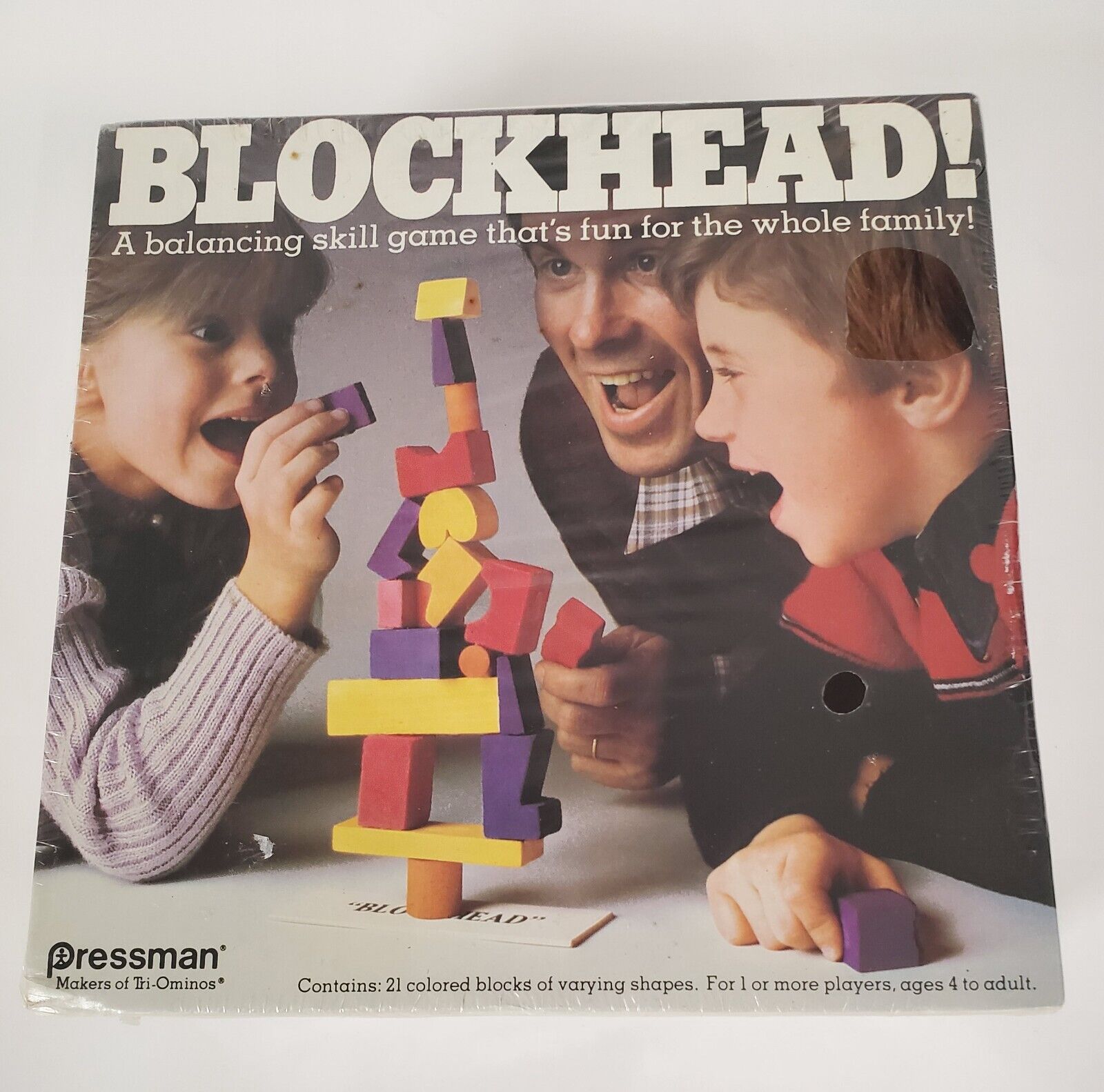 A vintage "BLOCKHEAD!" board game cover featuring two kids and an adult excitedly playing with a stack of colorful wooden blocks, with text indicating it is a balancing skill game for the whole family by Pressman.