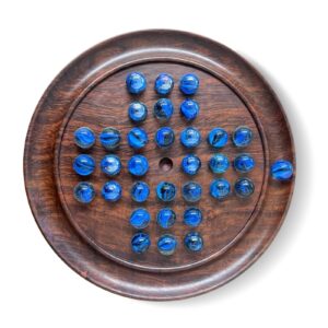A wooden solitaire board with blue marbles arranged in the starting pattern, with the center space empty, isolated on a white background.