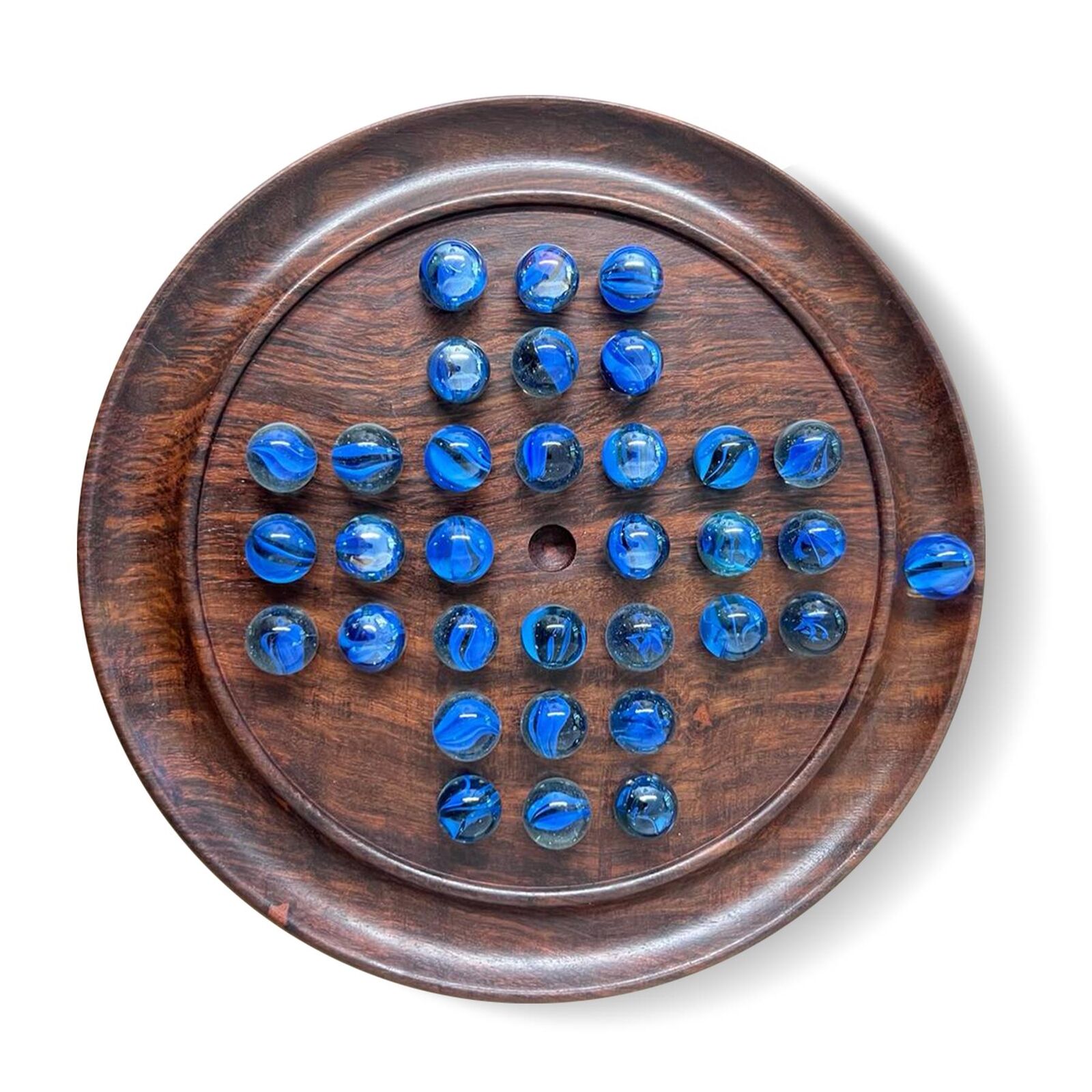 A wooden solitaire board with blue marbles arranged in the starting pattern, with the center space empty, isolated on a white background.