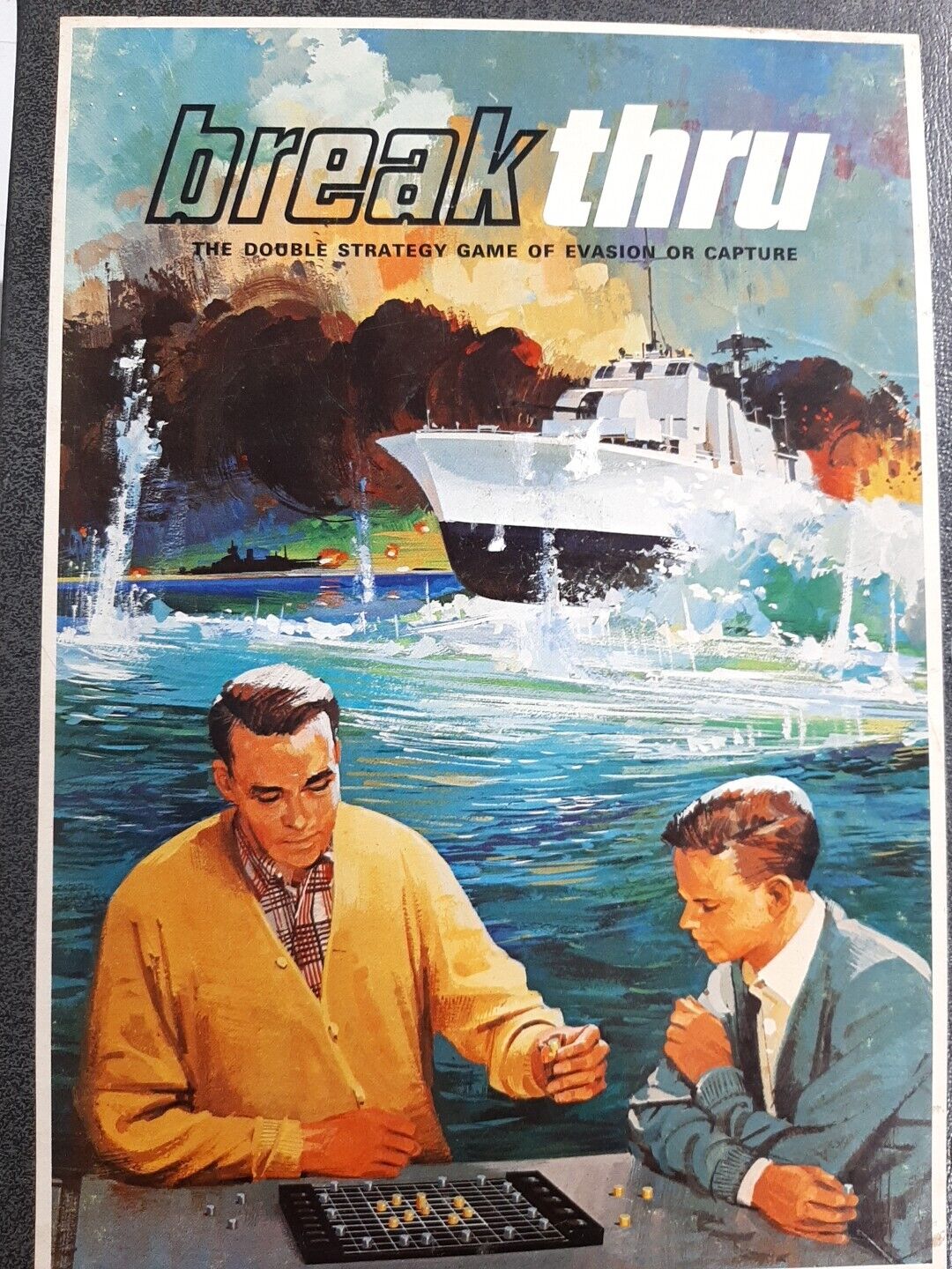 Vintage board game cover art for "breakthru" depicting two men playing a strategy game with a yacht and a scenic coastline in the background.