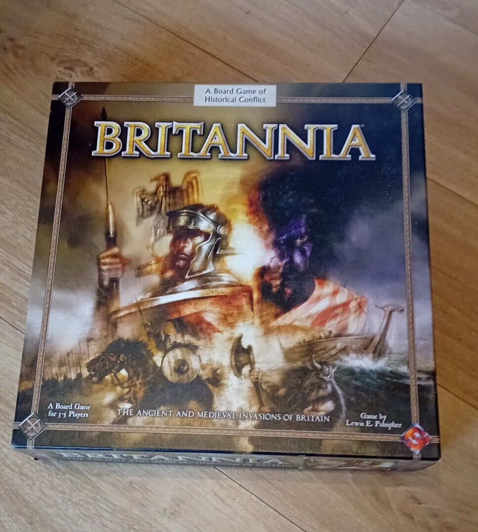 A board game titled "Britannia" placed on a wooden floor, featuring an illustration of historical warriors and a boat, indicating a theme of historical conflict in Britain.