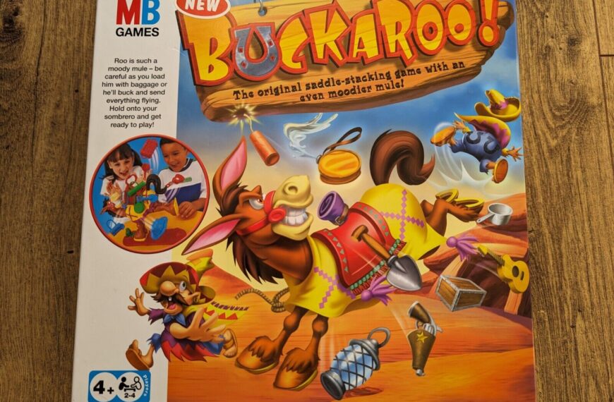 Board game "Buckaroo!" packaging with an animated bucking mule, flying objects, and a Western theme. The game's slogan "The original saddle-stacking game with an even moodier mule" is displayed, along with the MB Games logo and an image of two children playing the game. The packaging notes a 4+ age rating and is for 2-4 players.