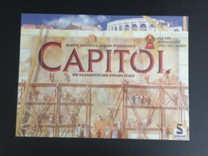 Board game cover for "CAPITOL" featuring an illustration of multiple people constructing classical Roman buildings with scaffolding, cranes, and the Colosseum in the background. Text includes the names "Alan R. Moon's & Aaron Weissblum's", "Die Baumeister der ewigen Stadt", and a label indicating "Spiel des Jahres" nominee for 2001. Schmidt Spiele logo is visible in the bottom right corner.