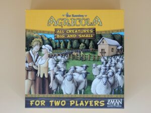 Alt text: Cover of the board game "Agricola: All Creatures Big and Small" featuring a cartoon illustration of a farm scene with a man and woman in period clothing standing in front of a flock of sheep, a barn, and fenced pastures, with the text "For Two Players" and the Z-Man Games logo at the bottom.