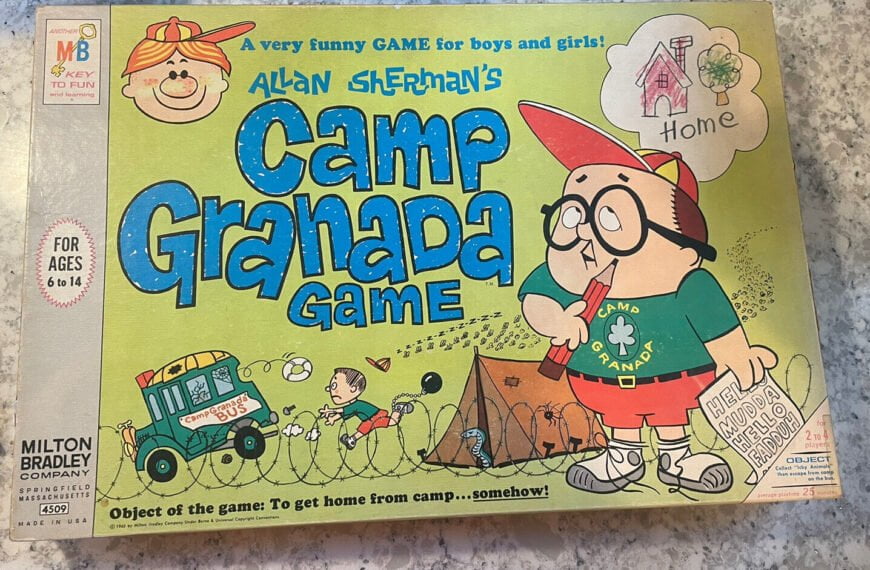 Vintage "Allan Sherman's Camp Granada Game" board game box cover featuring cartoon illustrations including a boy in camp attire with a thought bubble of a house labeled "Home," another child entangled in telephone wire, and a bus with "Camp Bunks" written on the side. Text on the box reads "A very funny GAME for boys and girls!," "For ages 6 to 14," "Milton Bradley Company Springfield Massachusetts," and "Object of the game: To get home from camp... somehow." The box shows signs of wear and a handwritten note.