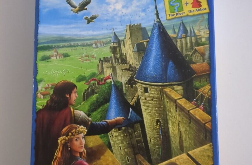 A photo of the board game "Carcassonne" by Klaus-Jürgen Wrede. The cover features a medieval landscape with a castle and two illustrated figures, a man and a woman, looking over a rampart. A crest with the game's name flies above them like a banner, with birds in the sky. Text on the cover states "Includes the mini expansions The River The Abbot" and "More than 10 million games and expansions sold." The Z-Man Games logo is in the bottom right corner.