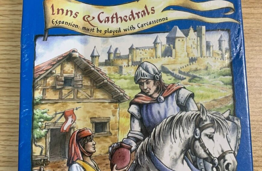 The image shows the cover of a board game named "Carcassonne: Inns & Cathedrals" by Klaus-Jürgen Wrede, published by Rio Grande Games. It features an illustration of a knight on horseback receiving something from a villager against a background of medieval buildings, with "Expansion: must be played with Carcassonne" written under the title.