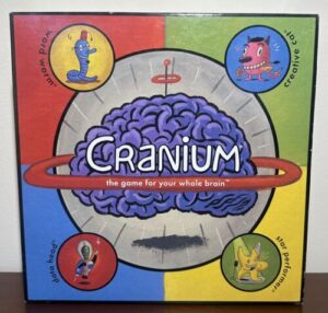 Box cover of the board game "Cranium" featuring a cartoonish brain and four colorful sections, each with a character representing different types of challenges: Word Worm, Data Head, Creative Cat, and Star Performer.
