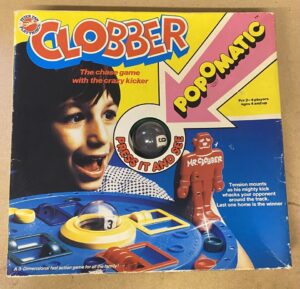 A vintage board game box for "CLOBBER POPOMATIC," featuring a smiling child, the game's colorful 3D playing surface with a clear dome containing a die, and a red figure named "MR. CLOBBER." Text on the box indicates it is a chase game for 2-4 players aged 4 and up, describing the gameplay and touting it as "A 3-Dimensional fast action game for all the family."
