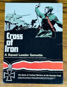 Cover of the "Cross of Iron" squad leader board game, featuring a stylized illustration of a soldier with raised fist in front of a tank and infantry, with the Iron Cross medal and a red and black stripe design on the lower part of the cover.
