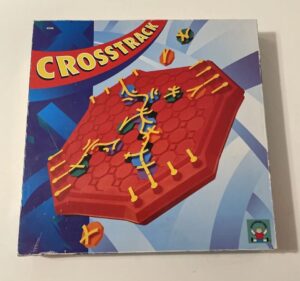 Box cover of the board game "Crosstrack," featuring a stylized depiction of a red hexagonal board with yellow tracks and multi-colored game pieces, set against a blue geometric background.