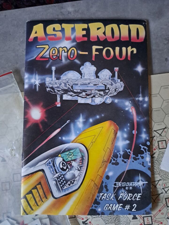 Cover of the board game "Asteroid Zero-Four," featuring a stylized outer space scene with an asteroid outfitted with domed structures, satellites, and a spaceship in the forefront, against a starry backdrop with the title in large red and yellow letters at the top. The bottom of the cover notes "Task Force Game #2."