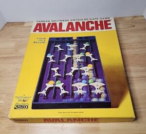 Old "Avalanche" board game by Parker Brothers, displayed in its original box with an image of the game in progress on the cover, placed on a wooden surface.