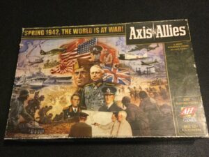 A weathered box cover of the board game "Axis & Allies," depicting various WWII imagery like military leaders, soldiers, planes, and ships, with the text "Spring 1942, The World is at War!" on top.