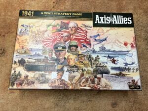 "Axis & Allies 1941 board game box cover featuring various World War II figures, scenes of battles on land, air, and sea, and a headline from 'The Daily News' about an invasion."