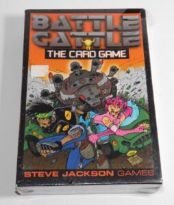 Alt text: A worn box of "Battle Cattle: The Card Game" by Steve Jackson Games, featuring colorful cartoon artwork with a male and female character and a mechanical bull in the background.