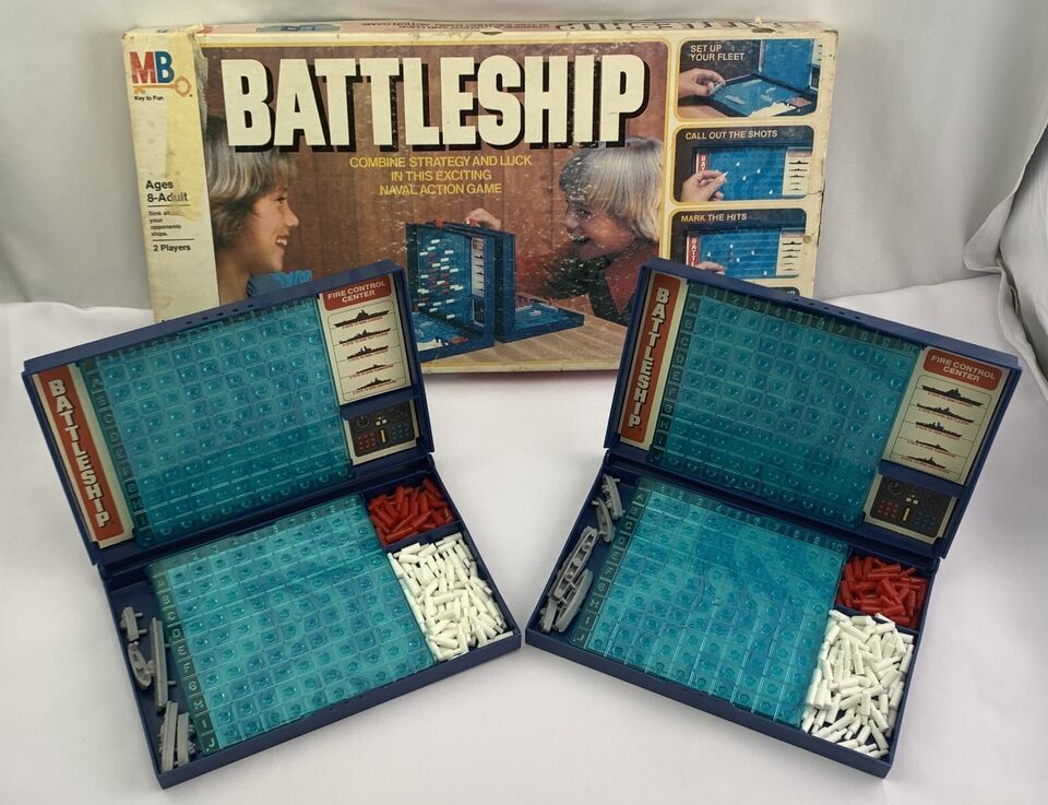 A vintage Battleship board game with its box in the background, and two foldable game boards open in the foreground showing blue grids and compartments with white and red pegs and miniature ship pieces.