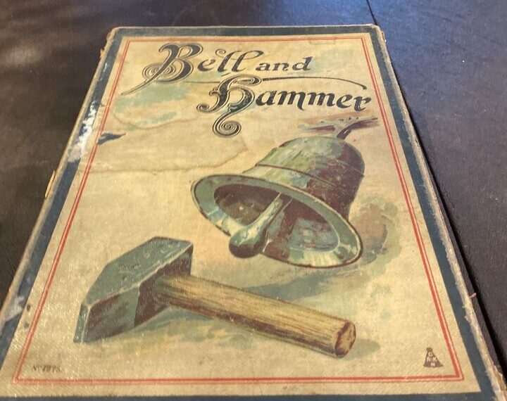 A worn antique board game titled 'Bell and Hammer' with a depiction of a bell and a hammer on its cover, resting on a wooden surface.