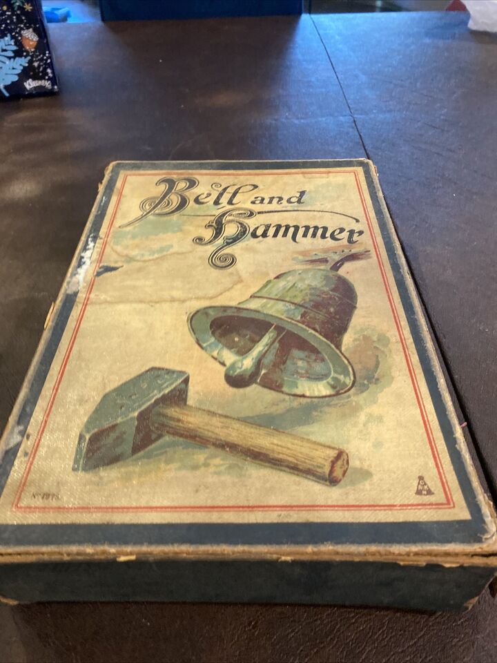 A worn antique board game titled 'Bell and Hammer' with a depiction of a bell and a hammer on its cover, resting on a wooden surface.