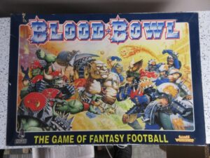Box art for Blood Bowl, the game of fantasy football, featuring a chaotic illustration of various fantastical creatures and humanoids engaged in a football-like game, with the title in bold red and blue at the top.